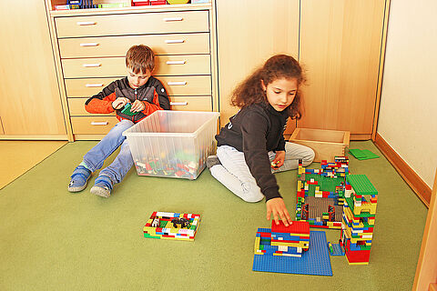 Ein Junge und ein Mädchen spielen am Boden mit LEGO-Steinen