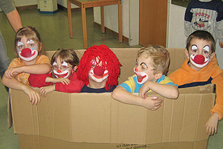 Fünf Kinder sitzen in einem großen Karton und sind als Clowns kostümiert