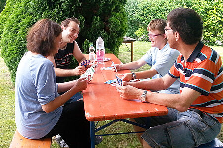 Bewohner des Ambulant betreuten Wohnens sitzen an einem Tisch im Garten und spielen Karten