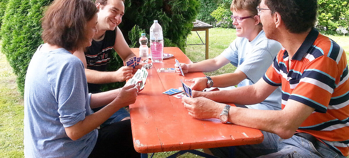 Bewohner des Ambulant betreuten Wohnens sitzen an einem Tisch im Garten und spielen Karten