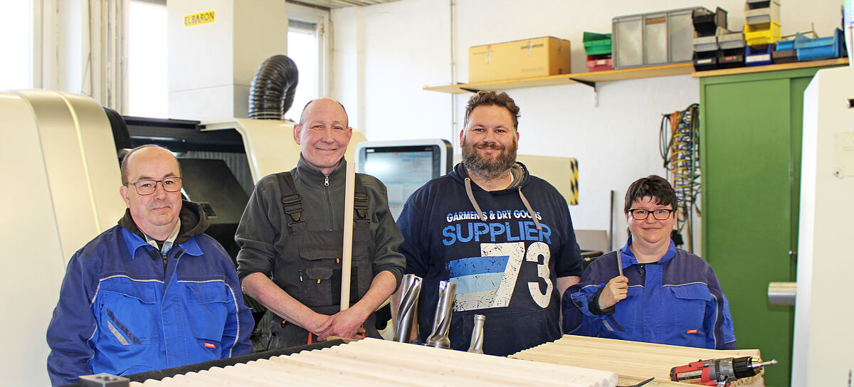 drei Werkstattmitarbeiter und eine Mitarbeiterin stehen nebeneinader vor einer Maschine und lächeln