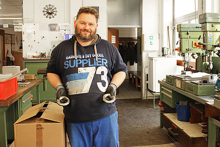 Werkstattmitarbeiter hält zwei Metallringe in den Händen, auf der rechten Seite sieht man Werkzeug und Maschinen
